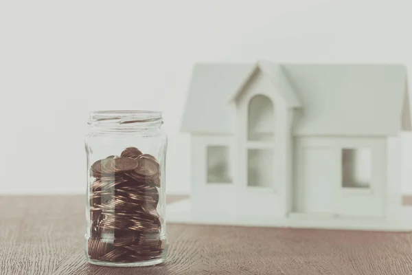 Frasco de moedas e pequena casa de madeira na mesa, economizando conceito — Fotografia de Stock