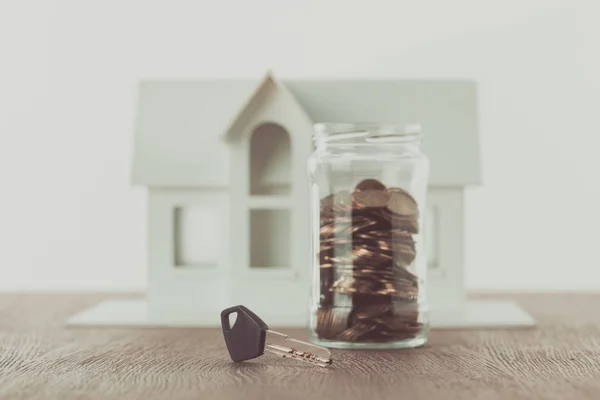 Ключ рядом банка монет на столе с маленьким домом на заднем плане, концепция экономии — стоковое фото