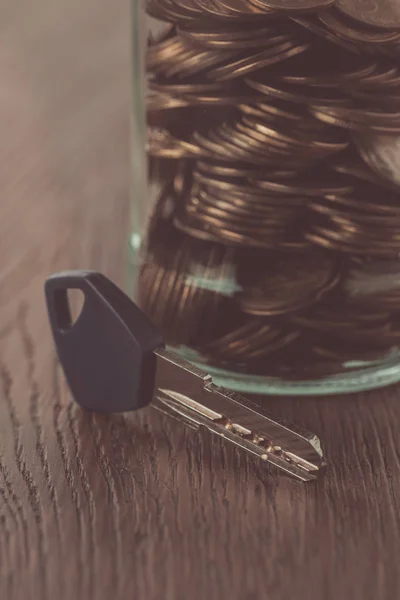 Ключ возле банки с монетами на деревянном столе, концепция экономии — стоковое фото
