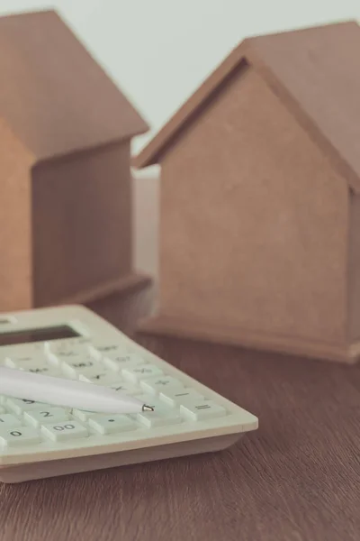Pequenas casas de madeira e calculadora com caneta em mesa de madeira, economizando conceito — Fotografia de Stock