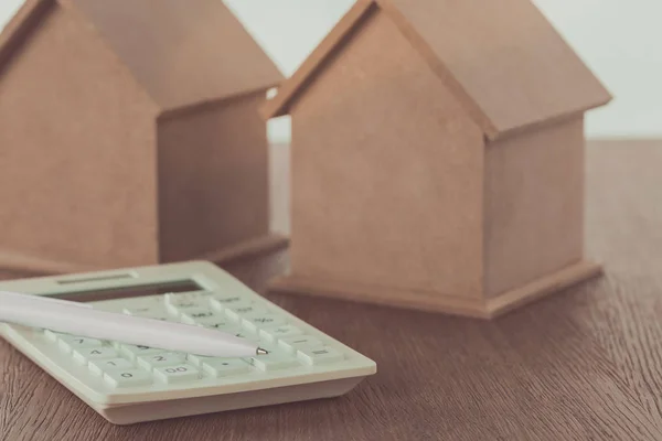 Pequenas casas de madeira e calculadora com caneta na mesa, economizando conceito — Fotografia de Stock