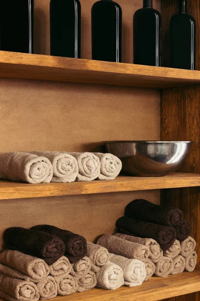 Tigela de metal vazia, toalhas enroladas e garrafas de vidro em prateleiras de madeira — Fotografia de Stock
