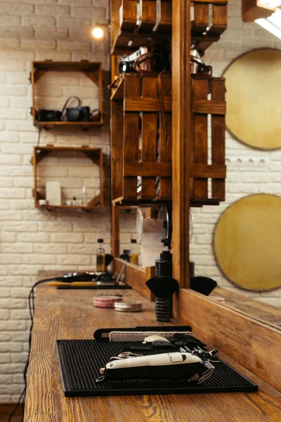 Professional barber tools on wooden shelf and mirror at modern barbershop — Stock Photo