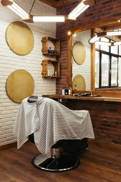 Interior de la barbería moderna y herramientas profesionales en estante de madera cerca del espejo - foto de stock