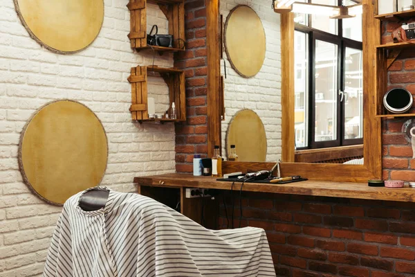 Современный интерьер парикмахерской и профессиональные парикмахерские инструменты на деревянной полке у зеркала — стоковое фото