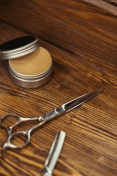 Vue rapprochée des ciseaux et du récipient avec de la cire à cheveux sur une table en bois — Photo de stock