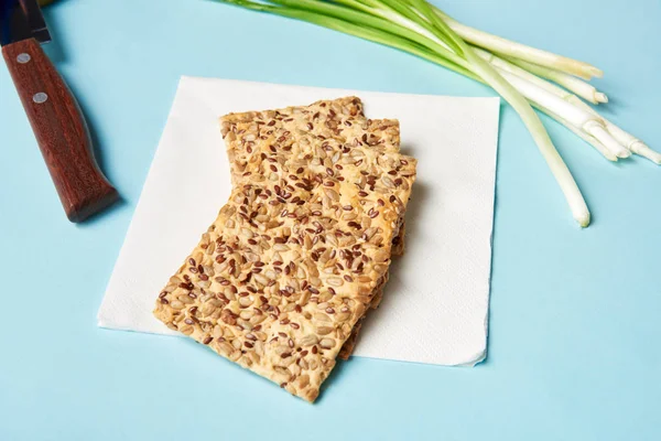 Vue rapprochée des biscuits aux graines, poireaux et couteau sur fond bleu — Photo de stock