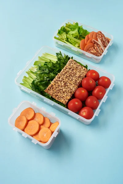 Close up view of arrangement of food containers full of healthy vegetables, meat slices and cookies on blue backdrop — Stock Photo