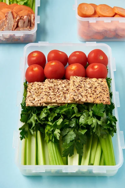 Close up view of arrangement of food containers full of healthy vegetables, meat slices and cookies on blue backdrop — Stock Photo