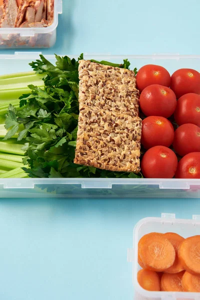 Close up view of arrangement of food containers full of healthy vegetables, meat slices and cookies on blue backdrop — Stock Photo