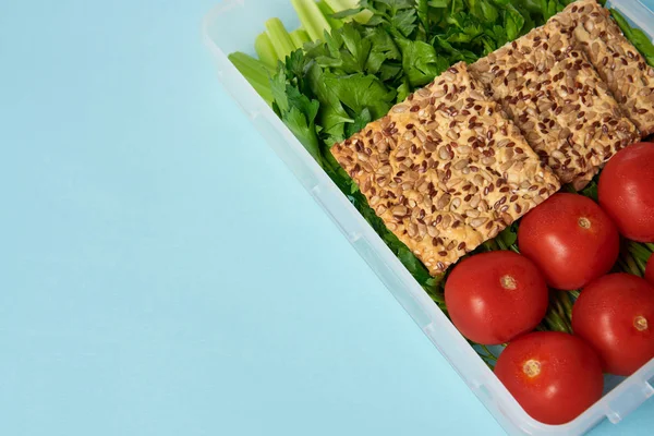 Vista de perto do recipiente de alimentos cheio de vegetais saudáveis e biscoitos isolados em azul — Fotografia de Stock