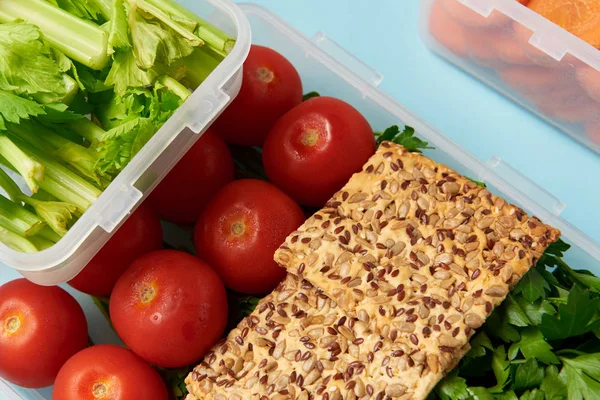 Vista de cerca de la disposición de contenedores de alimentos con verduras frescas y galletas aisladas en azul - foto de stock