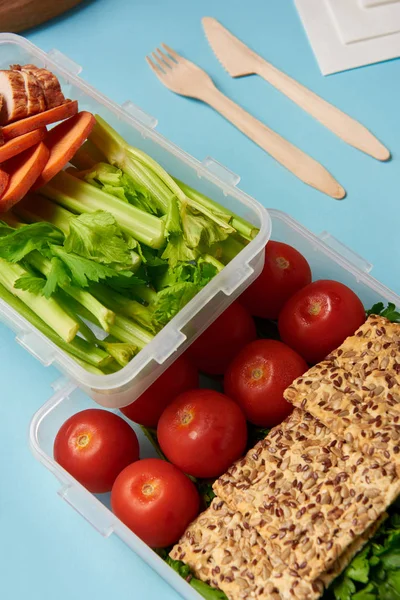 Vista de perto do arranjo de recipientes de alimentos com alimentos frescos e saudáveis e talheres isolados em azul — Fotografia de Stock
