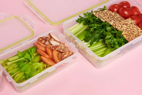 Close up view of healthy vegetables and cookies arranged in food containers on pink backdrop — Stock Photo