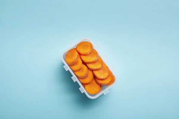 Vista superior do recipiente de alimentos cheio de fatias de cenoura saudáveis isoladas em azul — Fotografia de Stock