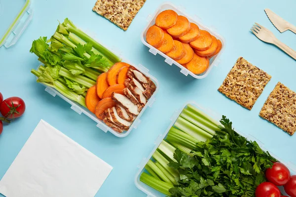 Vista superior do arranjo de recipientes de alimentos com alimentos frescos saudáveis, guardanapo e talheres isolados em azul — Fotografia de Stock