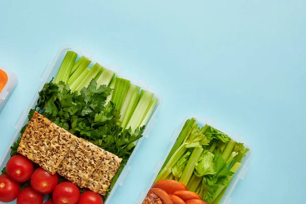 Top view of arrangement of food containers with fresh healthy vegetables and cookies with seeds isolated on blue — Stock Photo