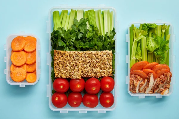 Top view of arrangement of food containers with fresh healthy vegetables, cookies and meat isolated on blue — Stock Photo