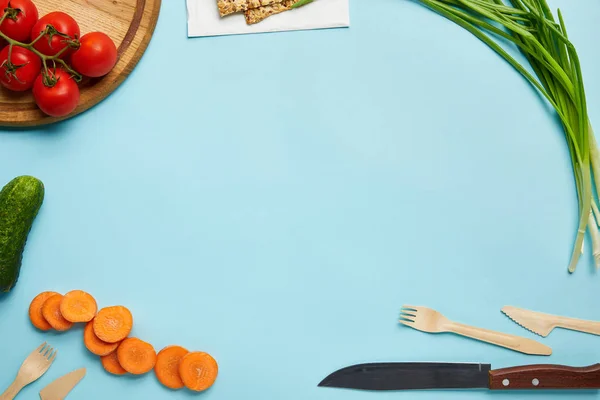 Top view of assorted fresh vegetables, cookies and cutlery isolated on blue — Stock Photo