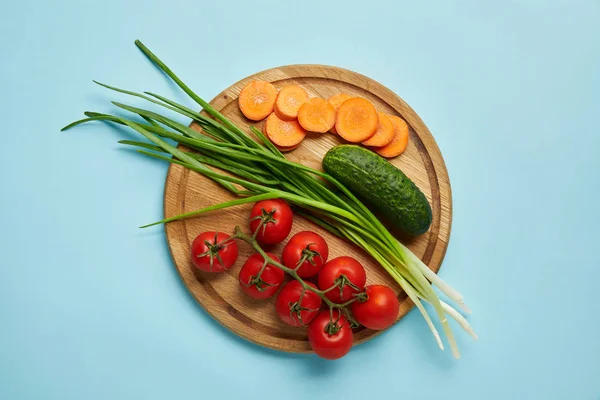 Top view of assorted fresh vegetables on wooden cutting board isolated on blue — Stock Photo