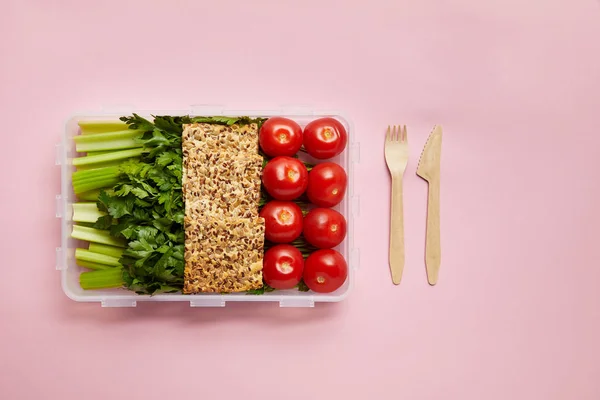 Tendido plano con alimentos saludables dispuestos en recipiente de alimentos y cubiertos aislados en rosa — Stock Photo