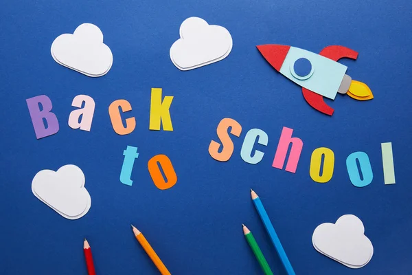 Vista dall'alto del lettering back to school con matite, nuvole e razzo su sfondo blu — Foto stock