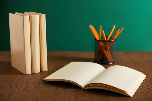 Відкритий підручник, книги та олівці на дерев'яному столі — стокове фото