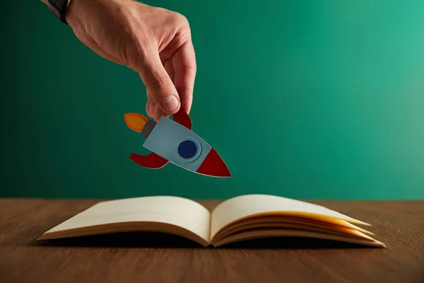 Cropped view of teacher holding rocket over open book — Stock Photo