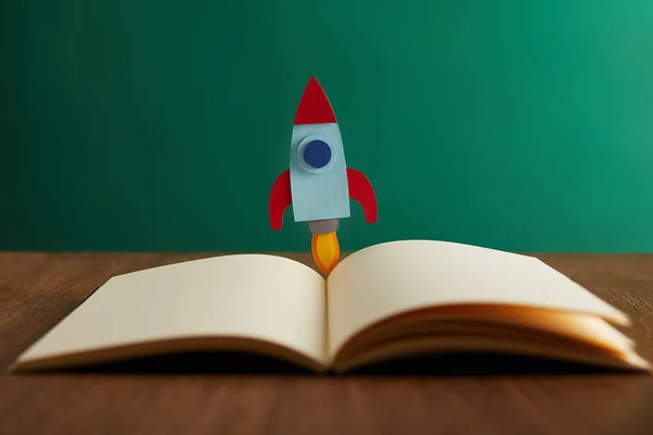 Открытая книга с красочной ракетой на деревянном столе — стоковое фото