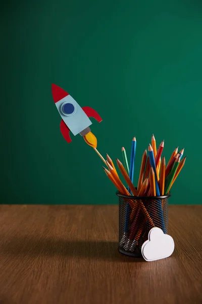 Crayons colorés, fusée, panneau nuage sur table en bois avec tableau noir sur fond — Photo de stock