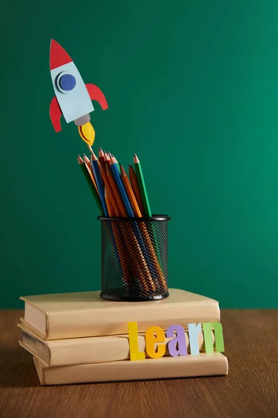 Libros, lápices de colores, cohete con aprender letras con pizarra en el fondo - foto de stock