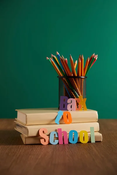 Красочные карандаши и книги на деревянном столе со школьными надписями — стоковое фото