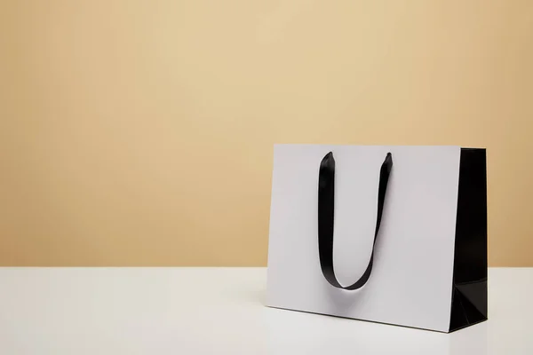 Una bolsa de compras blanca con asa negra sobre mesa blanca aislada en beige - foto de stock