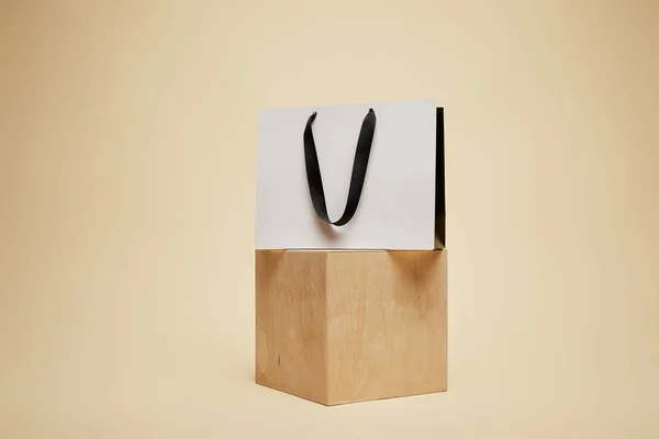 One shopping bag on wooden cube isolated on beige — Stock Photo