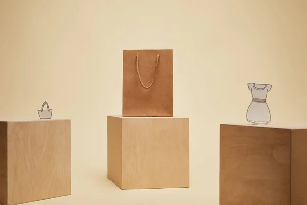 Paper shopping bag, paper bag and paper dress on wooden cubes isolated on beige — Stock Photo