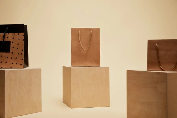 Три бумажных пакета для покупок на деревянных кубиках, изолированных на бежевом — стоковое фото