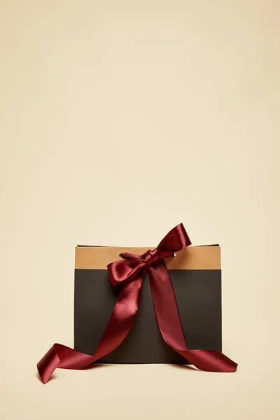 Fashionable black shopping bag with burgundy bow isolated on beige — Stock Photo