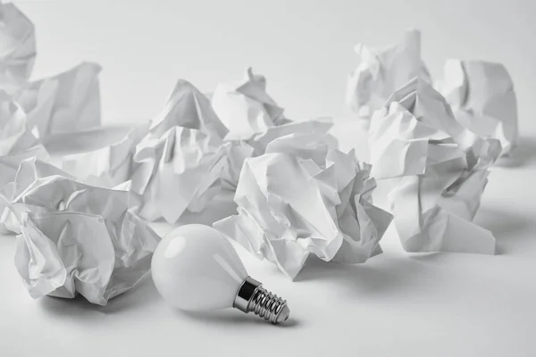 Close-up shot of energy saving light bulb with crumpled papers on white — Stock Photo