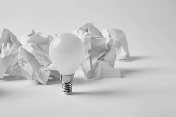Close-up shot of power saving light bulb with crumpled papers on white — Stock Photo