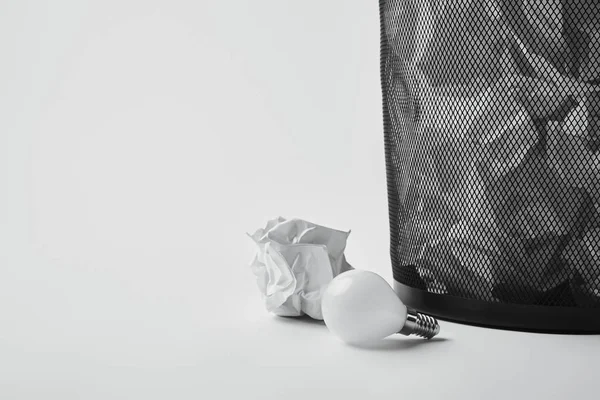 Close-up shot of power saving light bulb with crumpled papers in office trash bin on white — Stock Photo