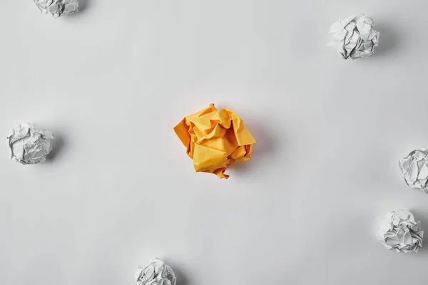 Top view of crumpled yellow paper surrounded with white crumpled papers on white surface — Stock Photo