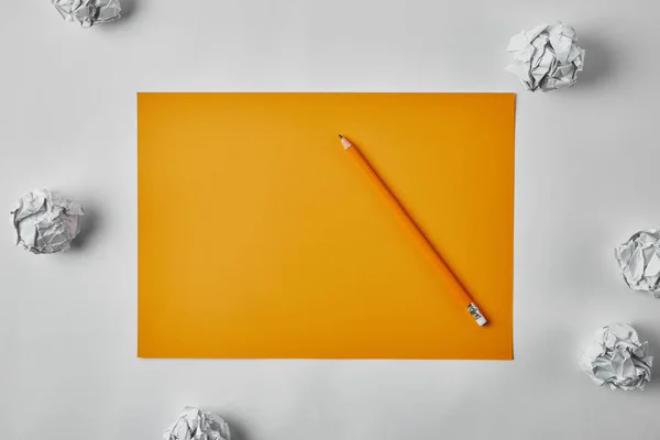 Vue du dessus du papier jaune vierge avec crayon entouré de papiers froissés sur la surface blanche — Photo de stock