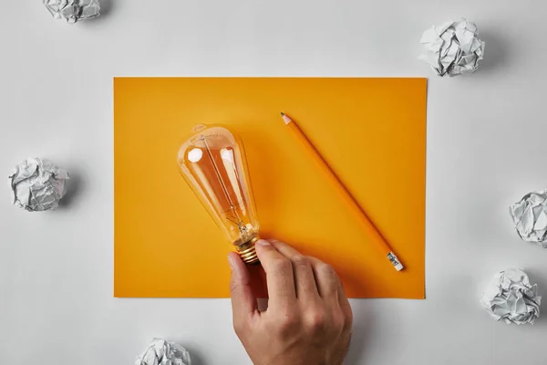 Foto ritagliata di uomo con lampada ad incandescenza su carta bianca gialla con matita circondata da carte spiegazzate su superficie bianca — Foto stock
