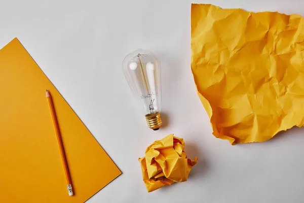 Vista superior de papeles amarillos con lámpara incandescente vintage y lápiz sobre superficie blanca — Stock Photo