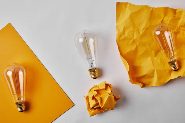 Vue du dessus des papiers jaunes avec lampe à incandescence vintage sur surface blanche — Photo de stock