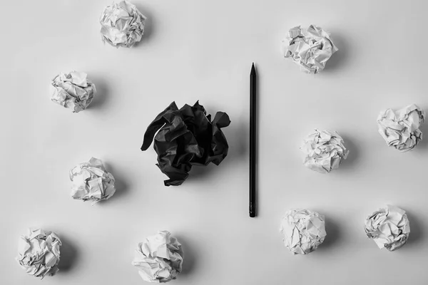 Vue de dessus des papiers noirs et blancs froissés avec crayon sur la surface blanche — Photo de stock