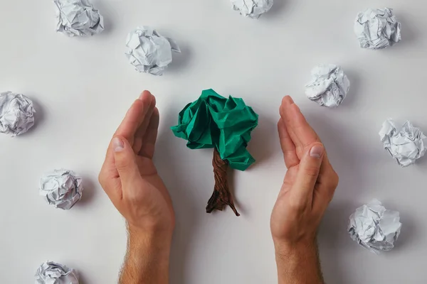 Cropped shot of man covering crumpled papers in shape of tree on white surface — Stock Photo