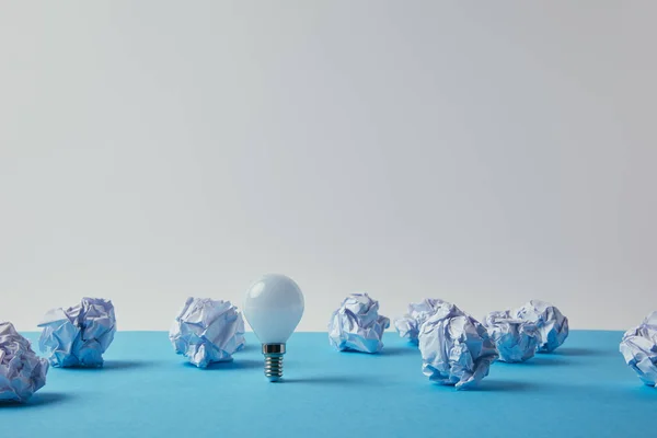Крупним планом знімок енергозберігаючої лампочки зі збитими паперами на блакитній поверхні — стокове фото