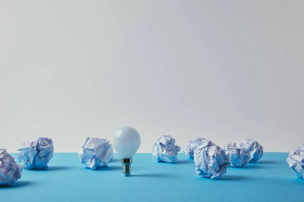 Close-up shot of power saving light bulb with crumpled papers on blue surface — Stock Photo