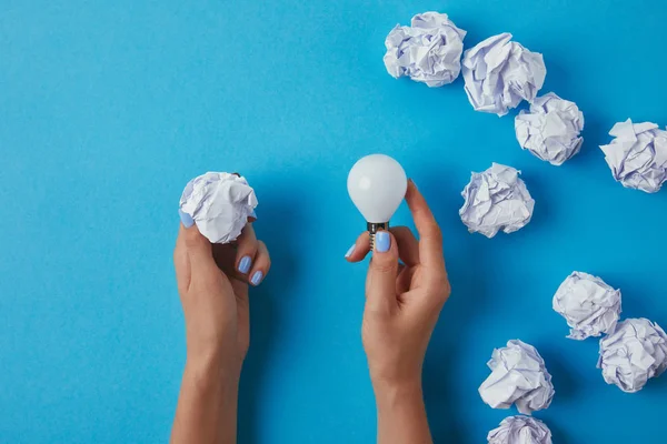 Tiro recortado de la mujer que sostiene la bombilla de ahorro de energía con papel arrugado sobre la superficie azul — Stock Photo